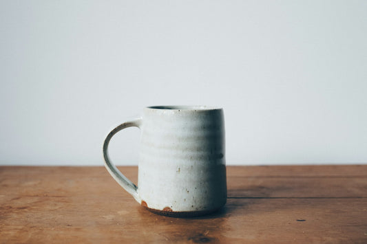 A single hand-thrown glazed stoneware mug standing on a bare wooden table.