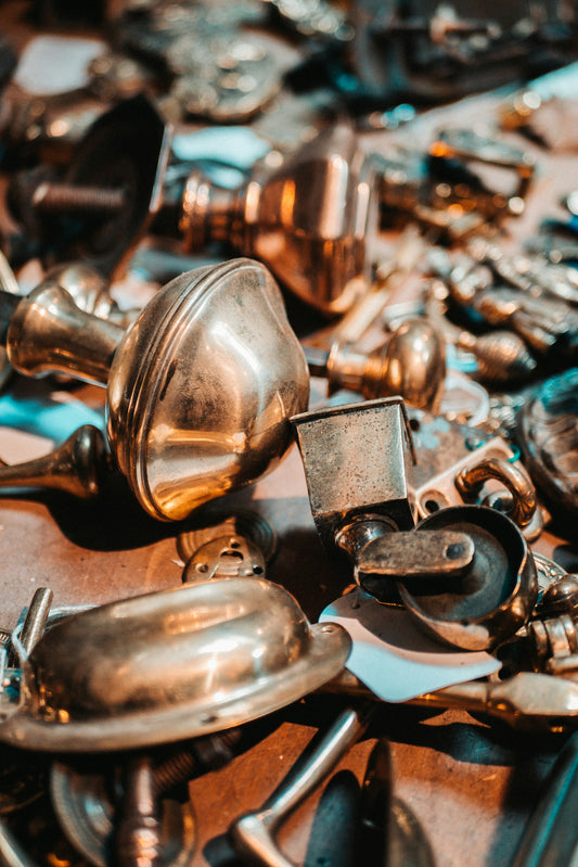 Antique brass door knobs and pulls in warm light, some bright, some gone dull with tarnish.