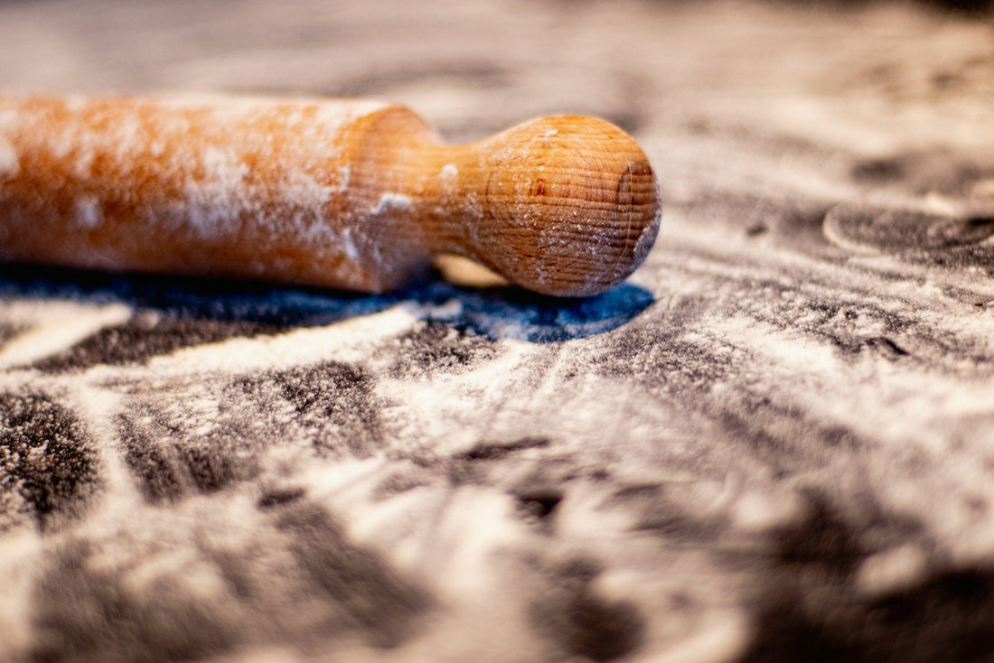 Macro of a turned wooden rolling pin handle dusted with flour, grain visible in warm light.