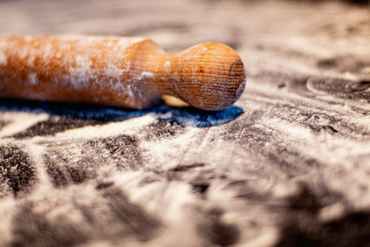 Macro of a turned wooden rolling pin handle dusted with flour, grain visible in warm light.