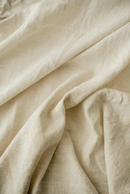 Close macro of the open flax weave, showing the slub and the soft folds of the linen.